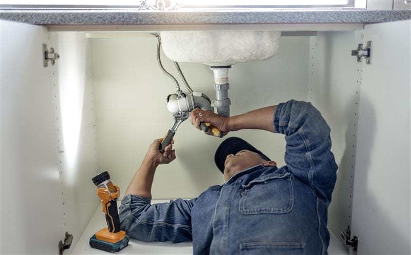 Plumber repairing pipes beneath a bathroom sink in Upper Darby