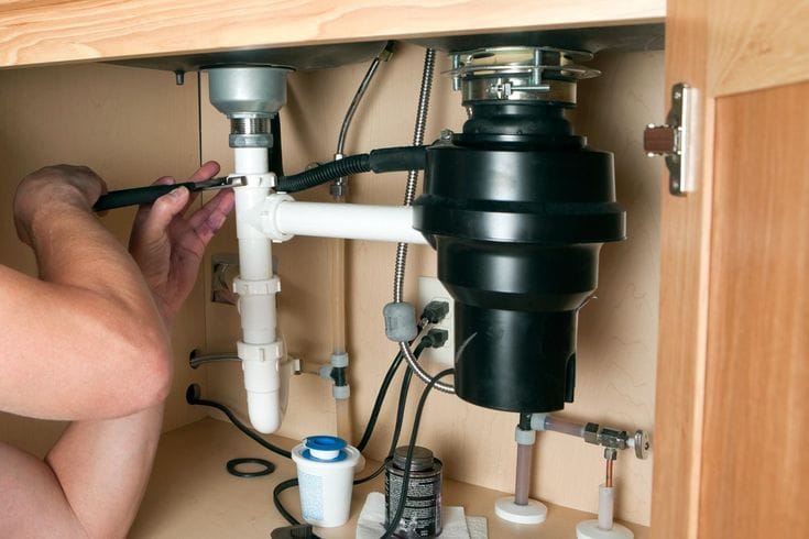 Plumber installing a garbage disposal beneath a kitchen sink in Upper Darby