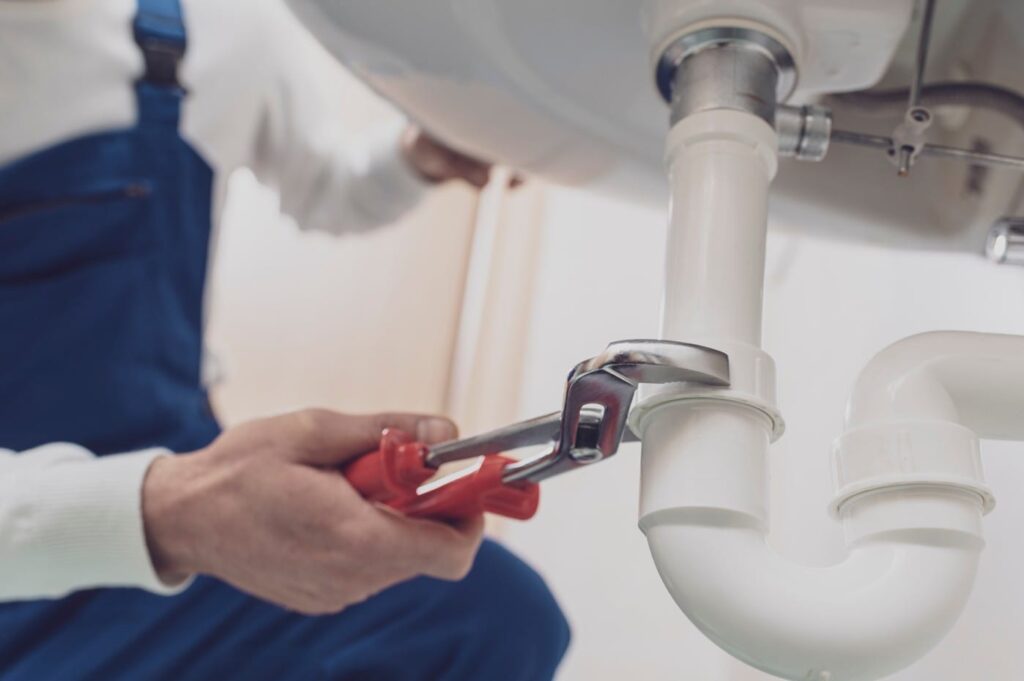 Plumber repairing a white drain pipe beneath a sink in Upper Darby