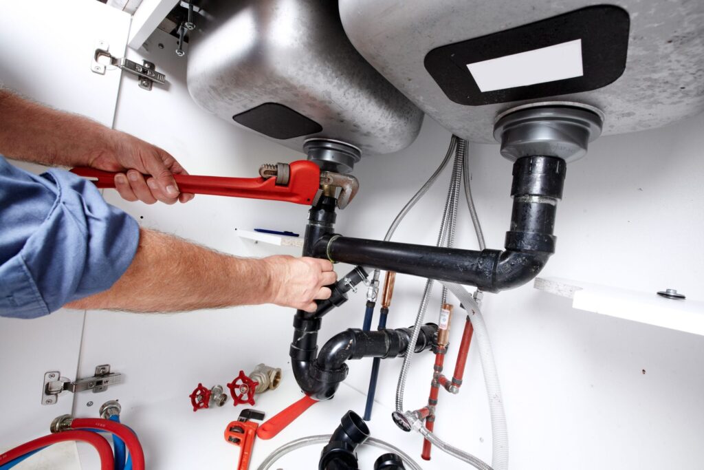 Plumber repairing drain pipes beneath a kitchen sink in Upper Darby